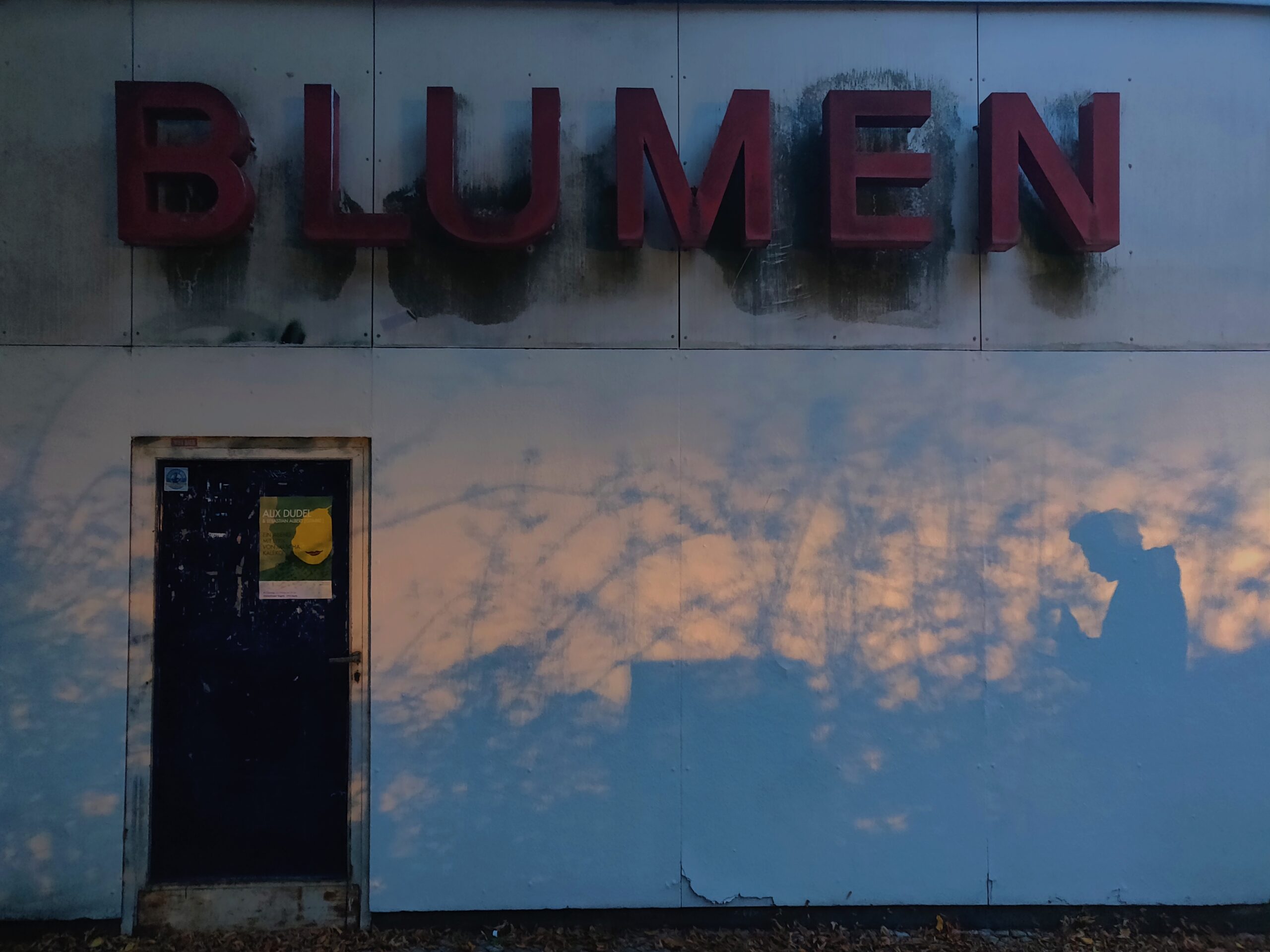 The word "Blumen" in all caps on a wall with a door