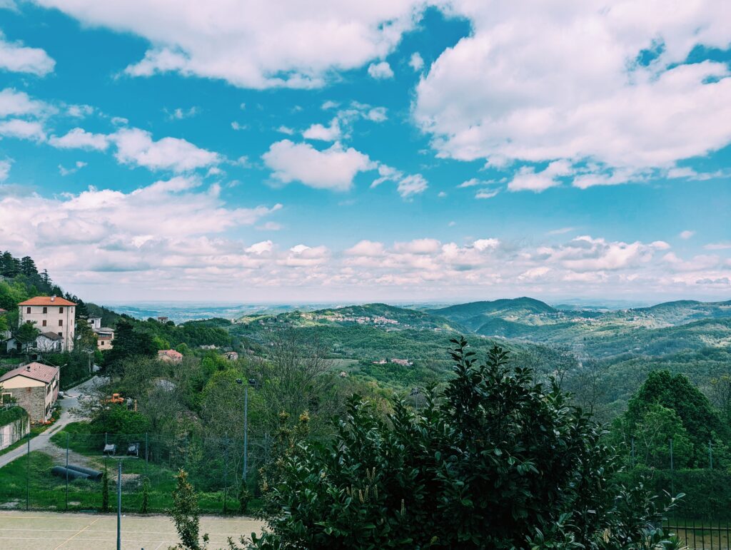 View from Cimaferle north. Some buildings in the foreground to the left, some hills and Po Valley in the background.