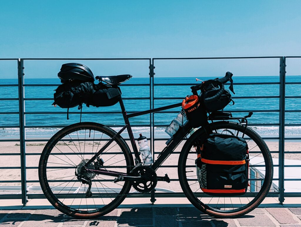My loaded touring bike leaned against a railing with the beach and the sea in the background