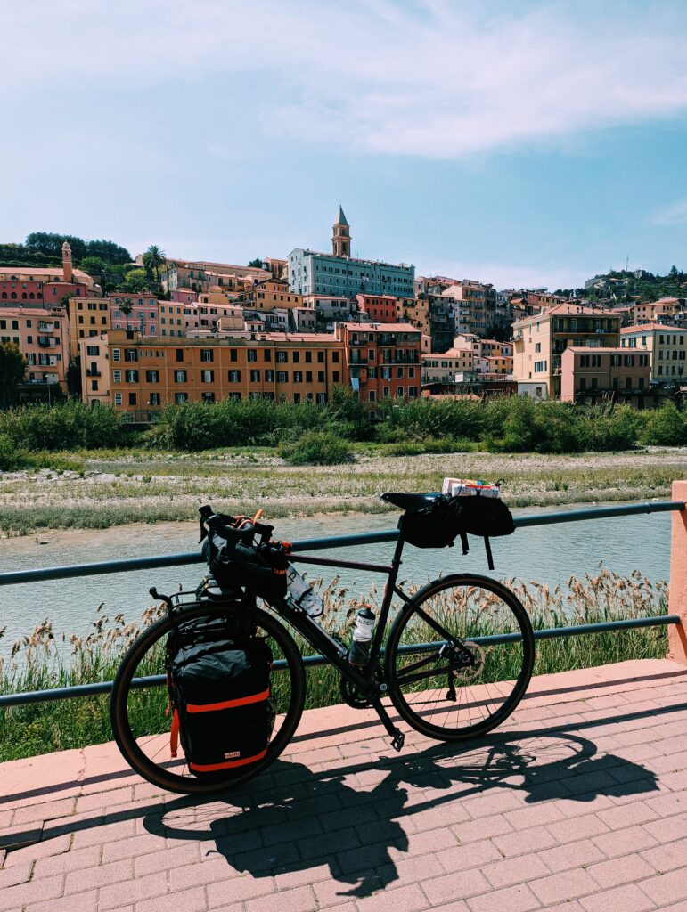 My loaded touring bike leaning against a railing in front of the river Roya with Ventimiglia Alta in the background