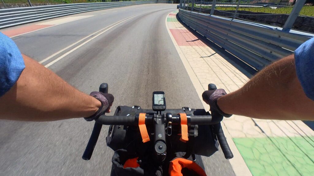 Action camera shot of my bike handlebars riding down a race track with painted curbs on either side and racing guard rails.