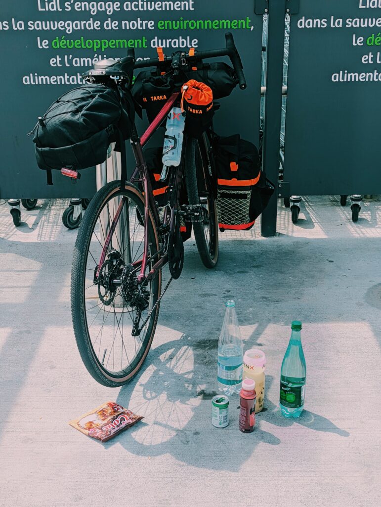 Bike with bags and panniers, several bottles of water and other drinks in the foreground on the floor