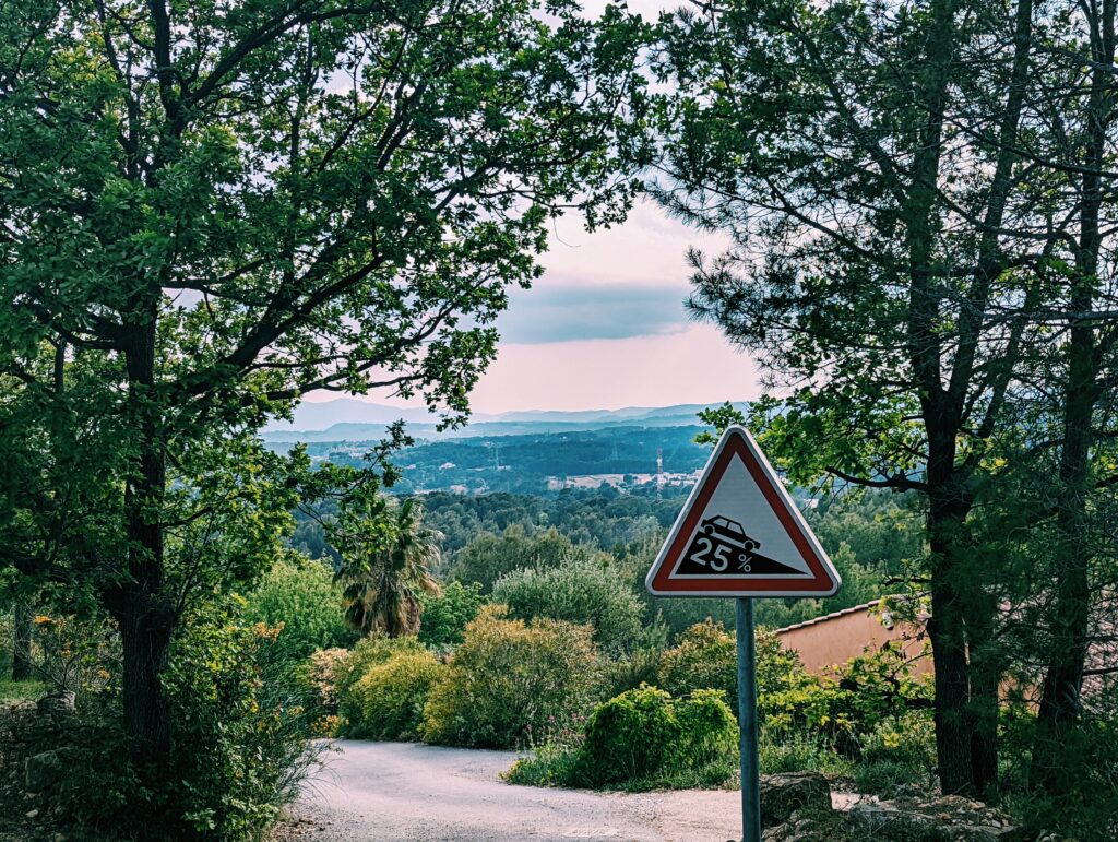 View over Draguignan framed by trees, traffic sign indicating a descent of 25%
