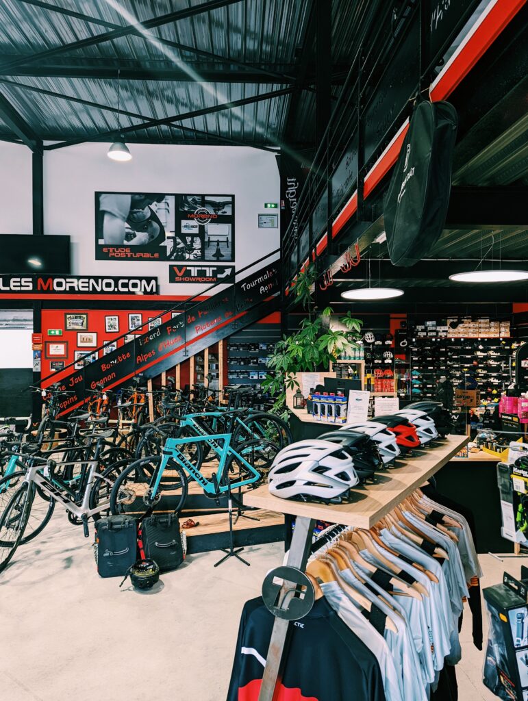 Interior of a bike shop in Perpignan, showing jerseys and helmets in the foreground and bikes in the background