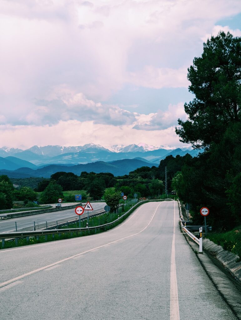 A road in the foreground and snow-covered Pyrenean peaks in tha background