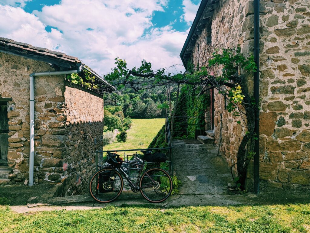 My bike inbetween two farm houses in the country side. A foresty hill in the background.