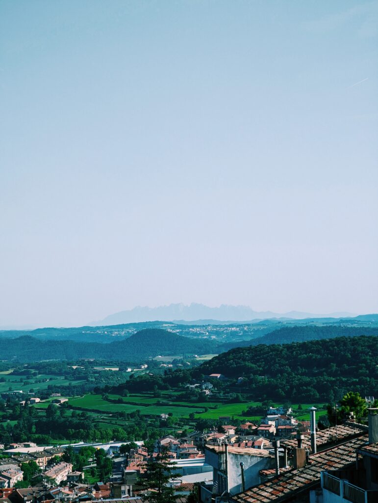 View over Berga in the foreground and Serra de Castelltallat in the background. Vast pale blue sky taking up more than half of the image.