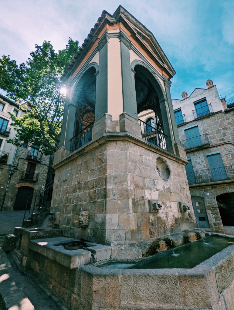 Font de la plaça de Sant Joan in Solsona with the sun peaking through a tree behind it