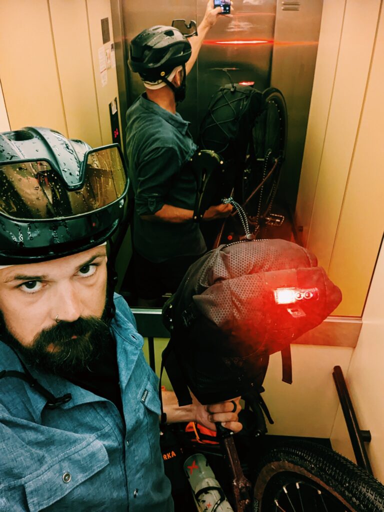 Selfie in an elevator with my bike crammed in. Rear light is on, my helmet and glasses are wet.