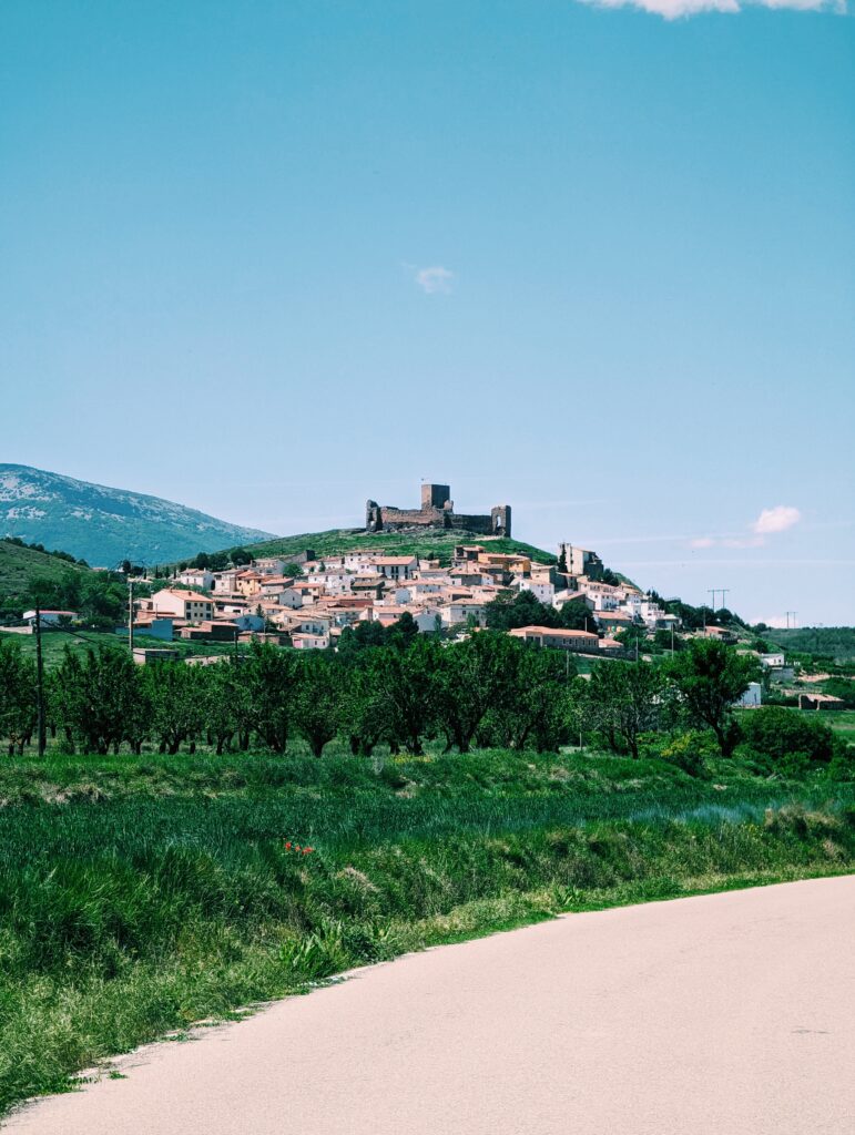 The town of Trasmoz on a hill in the middle ground surrounded by green fields and bushes, blue skies