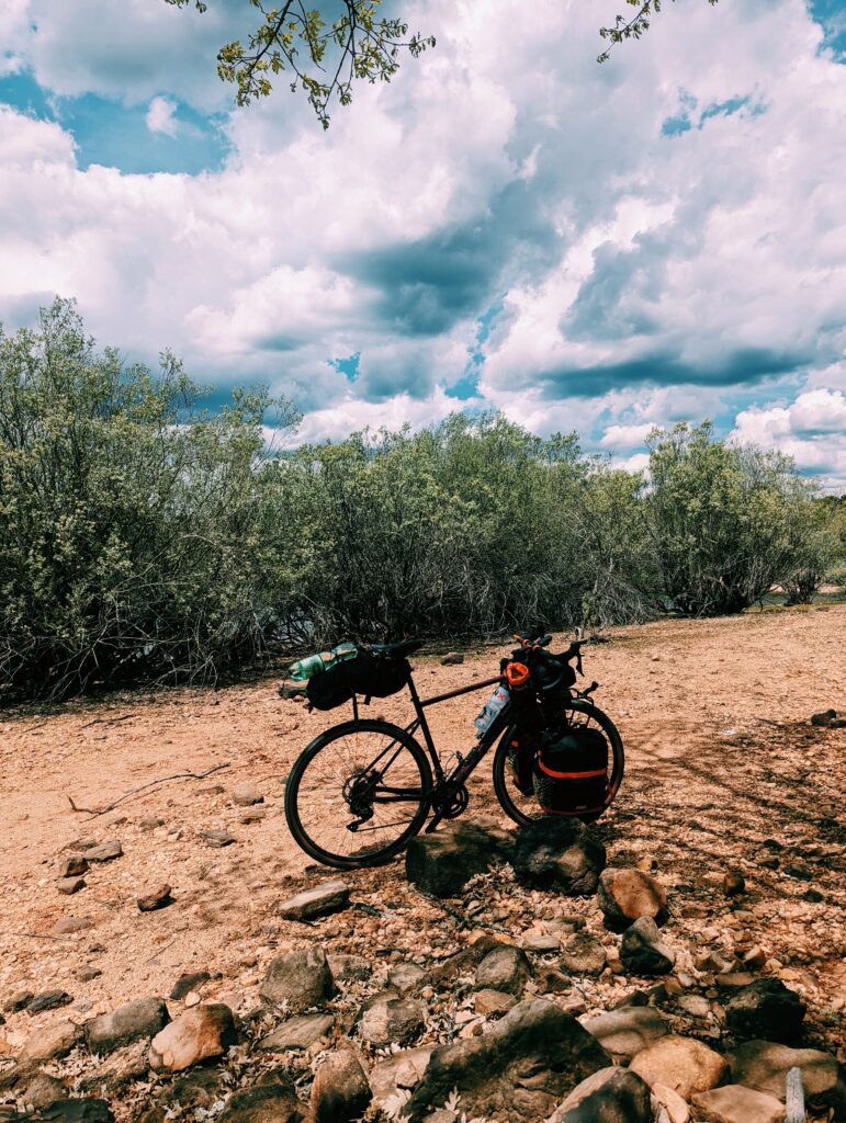 My bike on the shore of the artifical lake Embalse de Cuerda del Pozo. Some bushes in the middle ground and dark clouds in the sky.