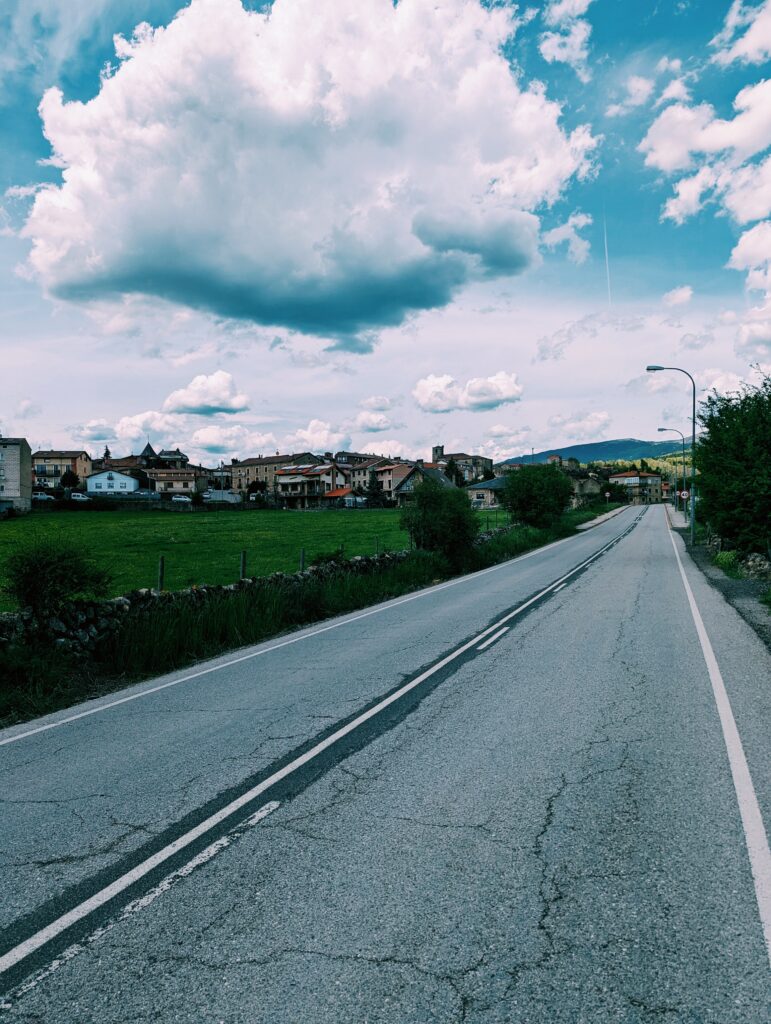 road in the foreground with a village in the background. Cloudy skies.