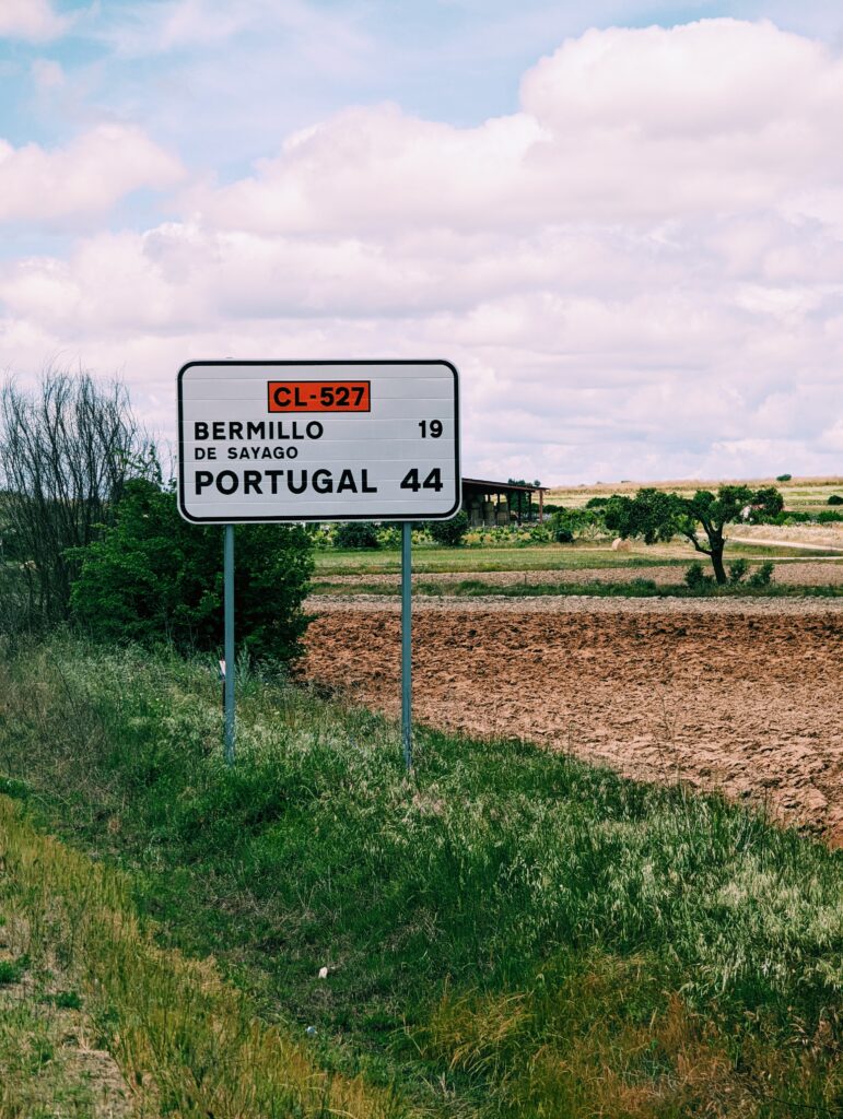 Street sign in a field saying it's 44km to Portugal.