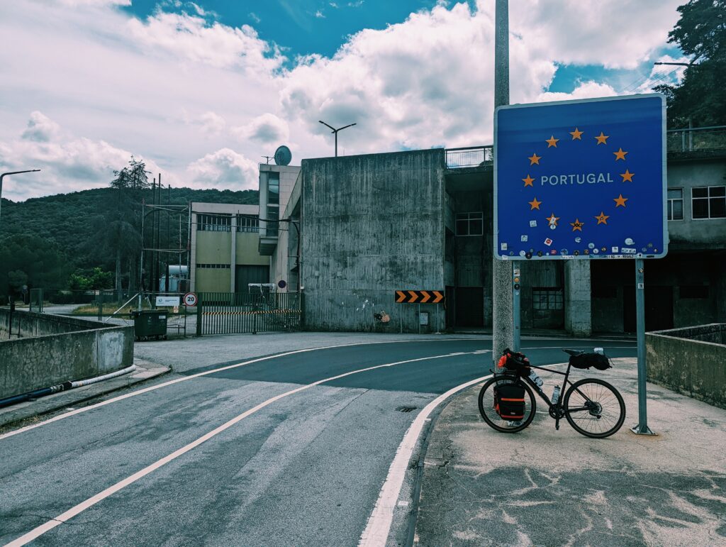 My bike leaned against the border sign of Portugal on the Miranda Dam. Concrete Dam structure in the background.