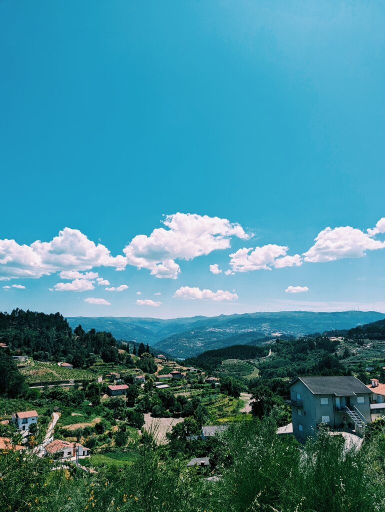 View inland with hills and valleys, some houses. long hanging clouds otherwise blue skies.